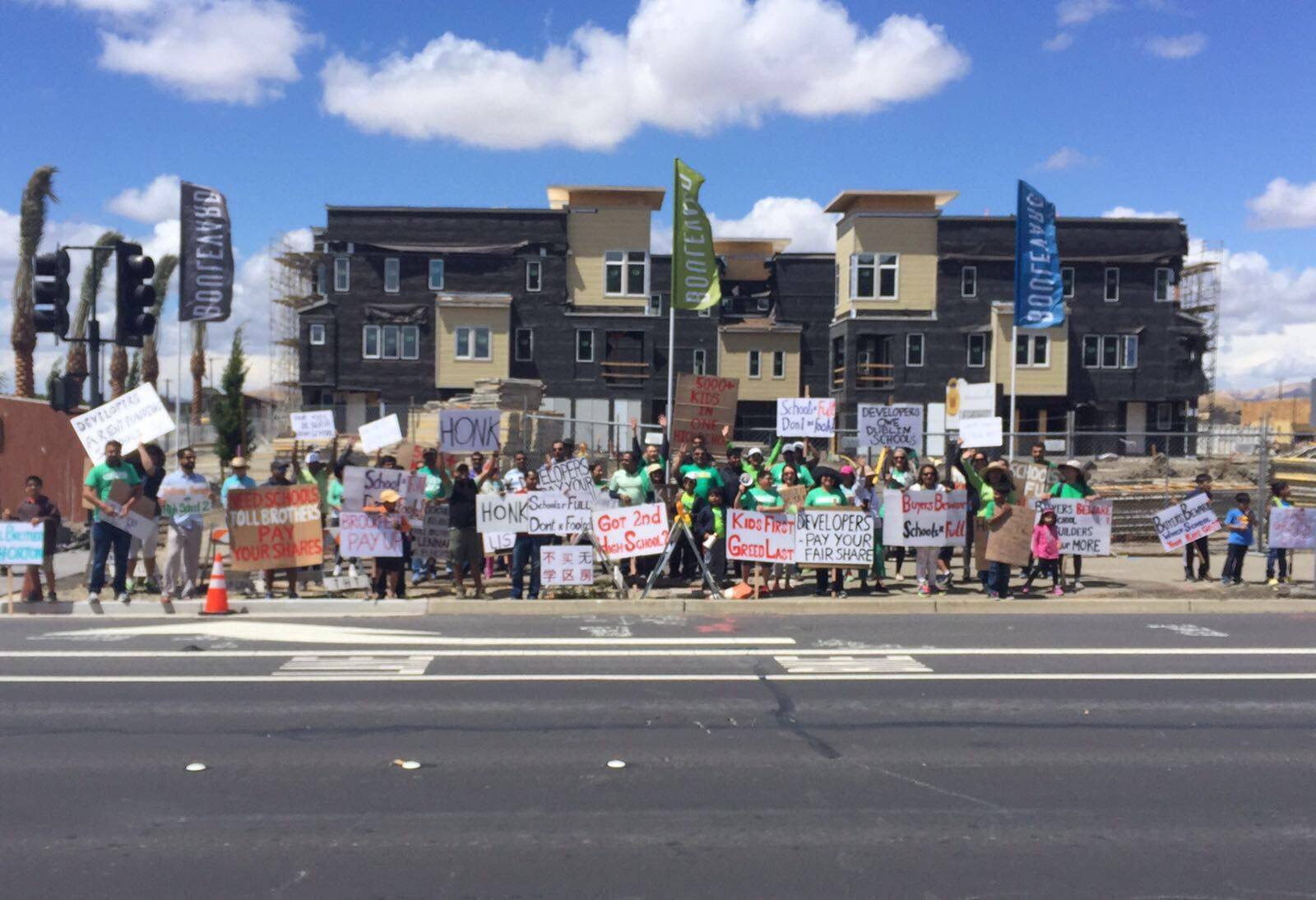 Dublin residents holding signs reading Got 2nd High School and Developers Owe Dublin Schools at a protest outside a new housing development